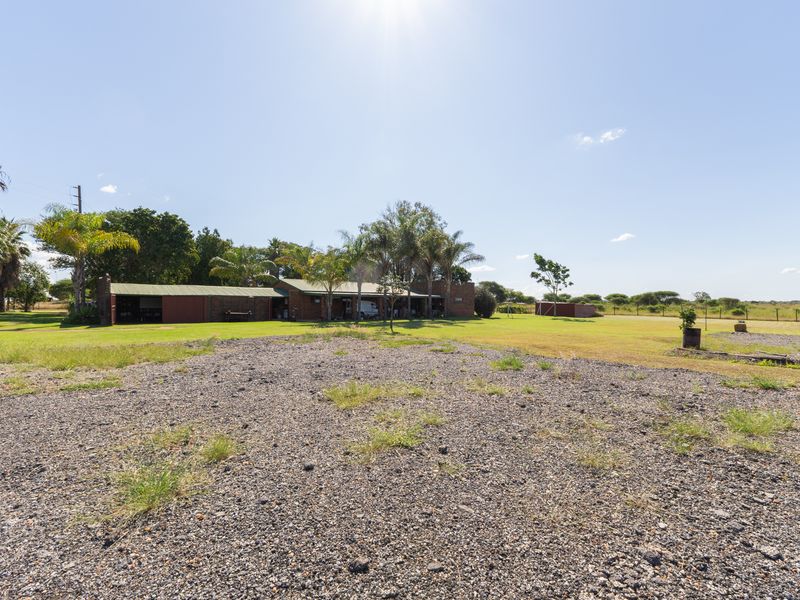Wide angle view of the farm property featuring a brick building with a metal roof, covered patio area, and expansive gravel driveway.