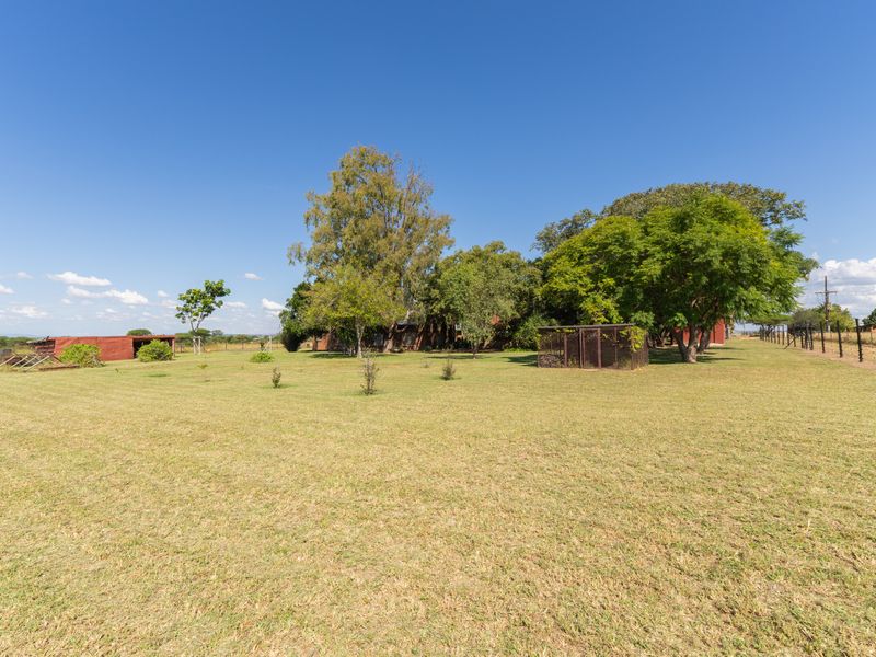 Expansive open garden area featuring mature trees, perimeter fencing, and a small outbuilding on a rural farm property.