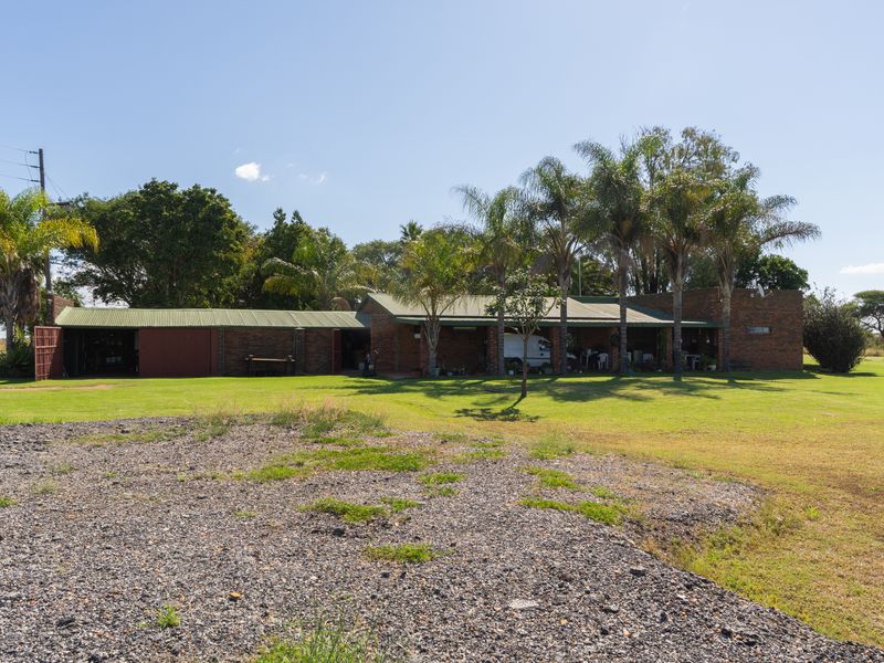 Rear view of a brick farmhouse featuring a covered patio area, corrugated metal roofing, and expansive surrounding lawn.
