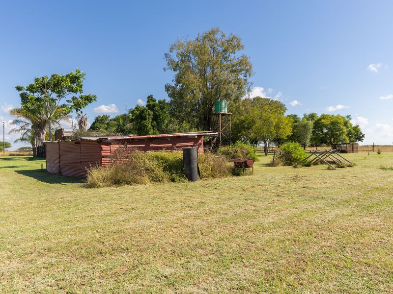 A view of a farm property featuring a corrugated iron shed and a raised water storage tank set within a large open field.