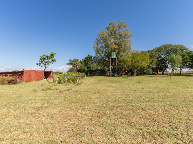 Expansive farm grounds featuring a metal storage shed, a raised water tank, and mature trees under a clear blue sky.