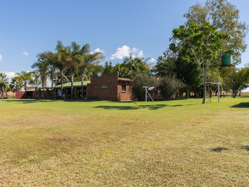 A view of the rear of the farm house featuring a brick exterior, covered patio area, and a raised water tank set within a large garden.