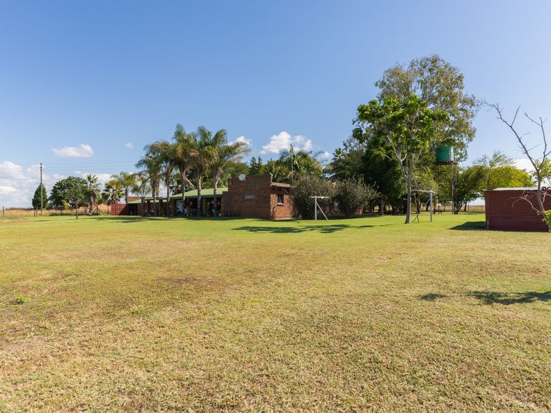 A wide view of the rear farm property featuring a brick dwelling with a covered patio, expansive lawn, and a water tank.
