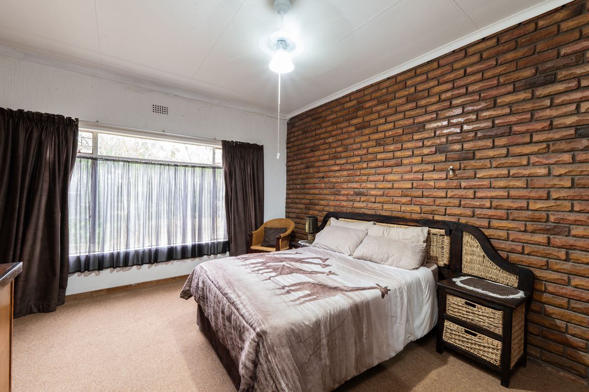 A bedroom featuring a prominent exposed brick feature wall, carpeted flooring, and a large window providing natural light.