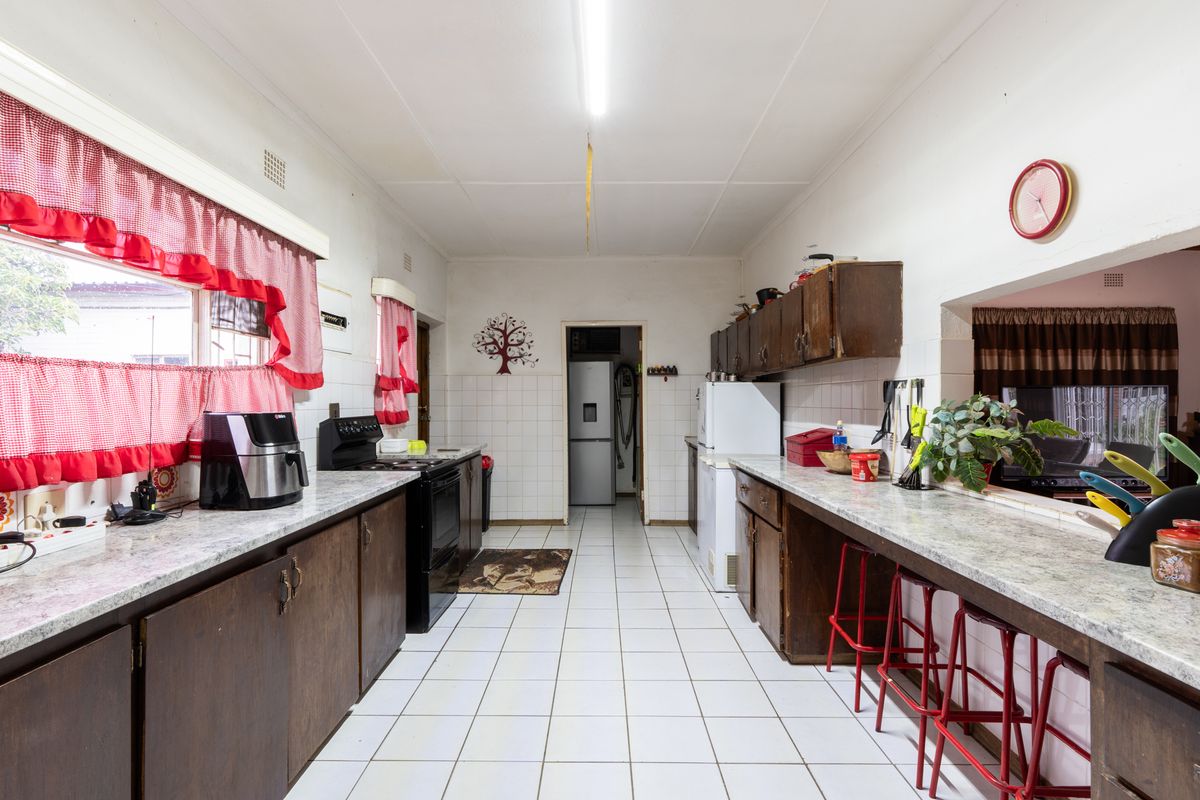 A functional kitchen featuring dark wooden cabinetry, laminate countertops, tiled flooring, and a breakfast bar pass-through window connecting to the adjacent living area.