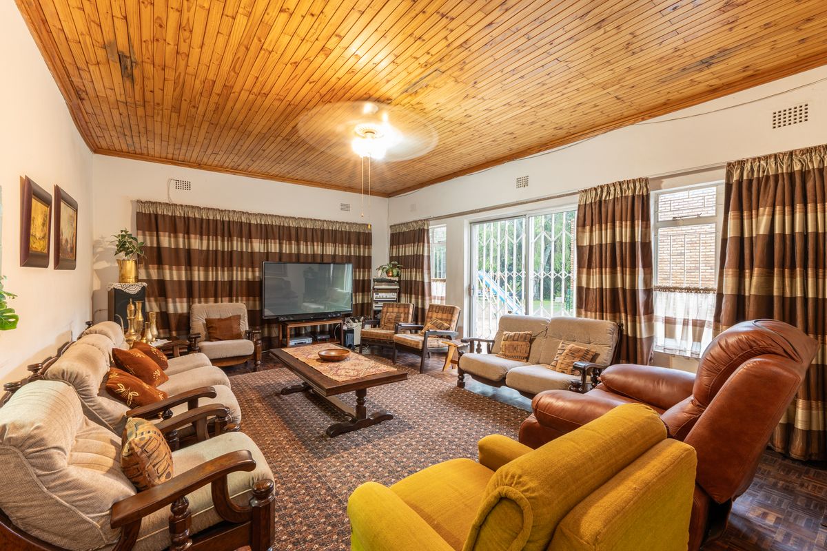 A spacious living room featuring a high wood-paneled ceiling, large windows with security gates, and direct access to the outdoor area.