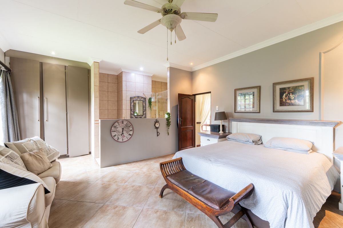 Spacious bedroom featuring tiled flooring, a ceiling fan, built-in cupboards, and an open-plan en-suite bathroom area with a glass-enclosed shower.