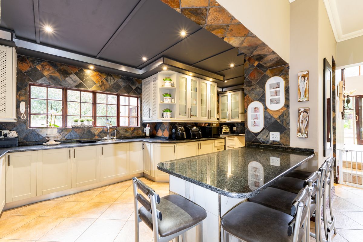 A well-appointed kitchen featuring granite countertops, custom cabinetry, slate tile backsplash, and a central breakfast island with integrated seating.