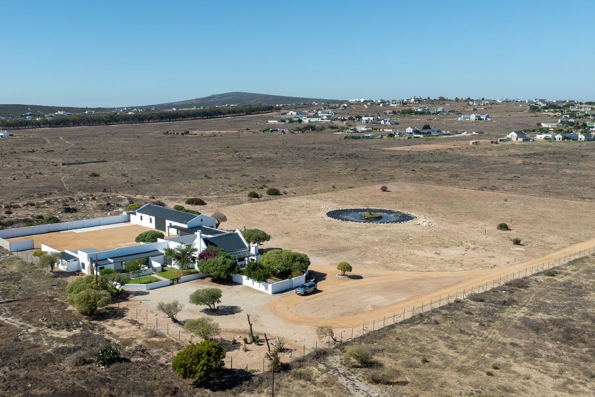 Aerial view of a rural property featuring a main dwelling with a courtyard, perimeter fencing, and a circular water reservoir on the grounds.