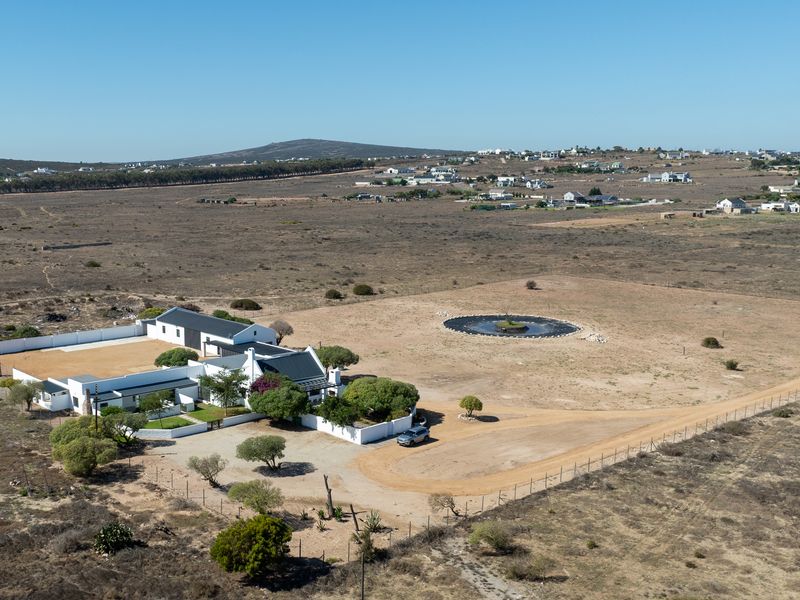 Aerial view of a rural property featuring a main dwelling with a courtyard, perimeter fencing, and a circular water reservoir on the grounds.