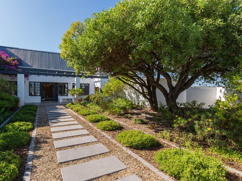 A well-maintained front entrance featuring a stone paver walkway, established garden landscaping, and a covered pergola structure.