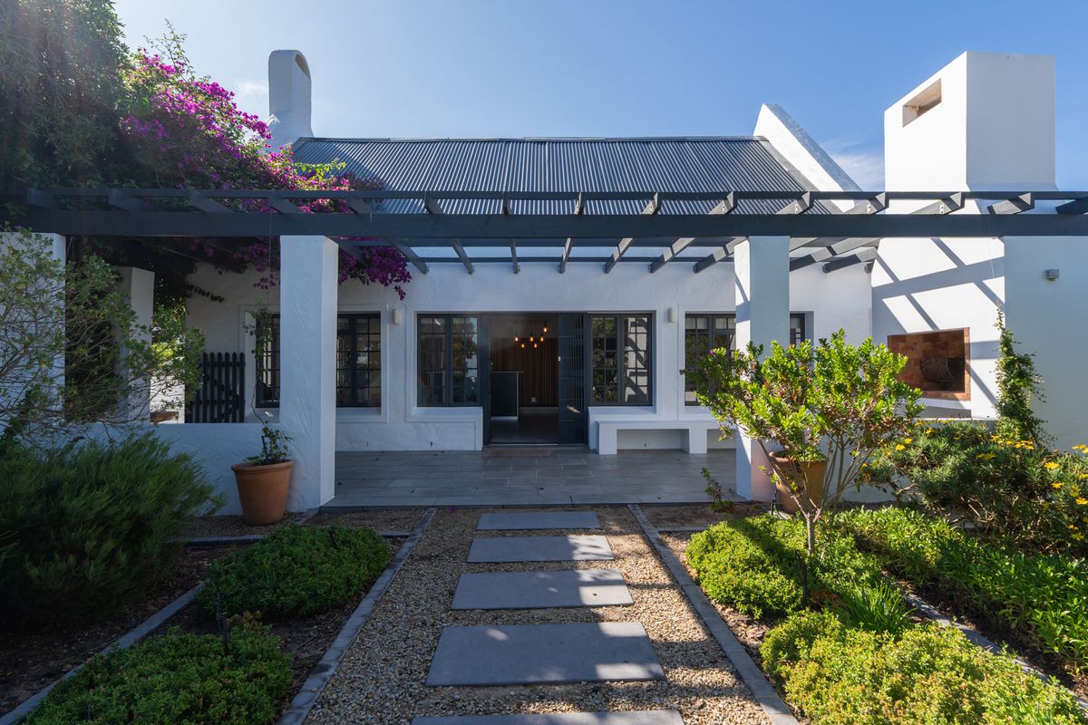 A beautifully maintained rear patio featuring a pergola, stone paving, and a built-in fireplace, overlooking a landscaped garden.