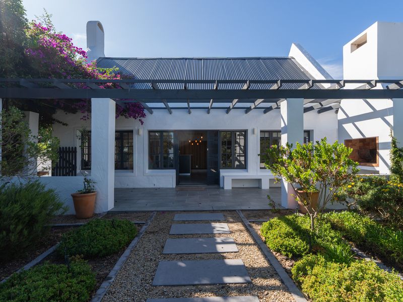 A beautifully maintained rear patio featuring a pergola, stone paving, and a built-in fireplace, overlooking a landscaped garden.