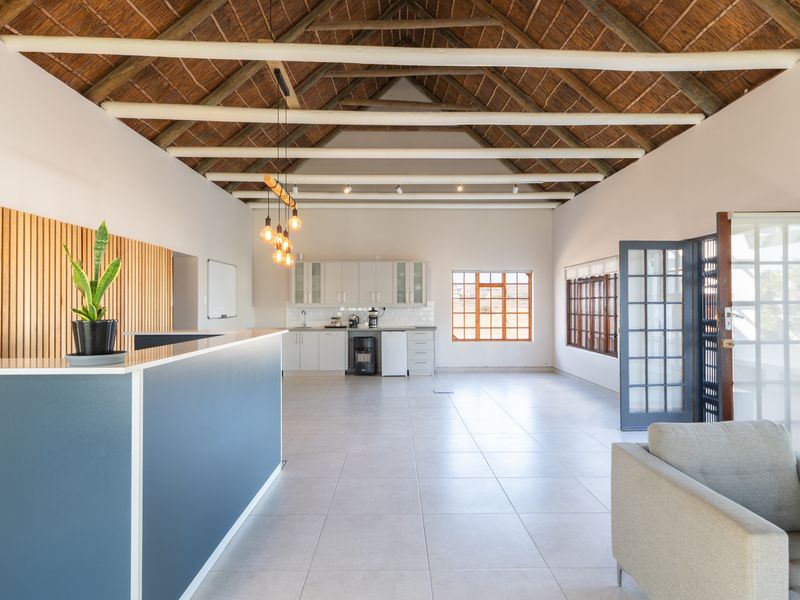 Spacious open-plan living area featuring a high vaulted thatched ceiling with exposed beams, tiled floors, and a modern kitchen with integrated cabinetry.