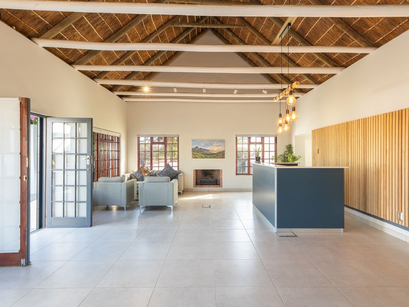 Spacious living area featuring a high thatched ceiling with exposed timber beams, tiled floors, a built-in fireplace, and modern timber slat wall detailing.