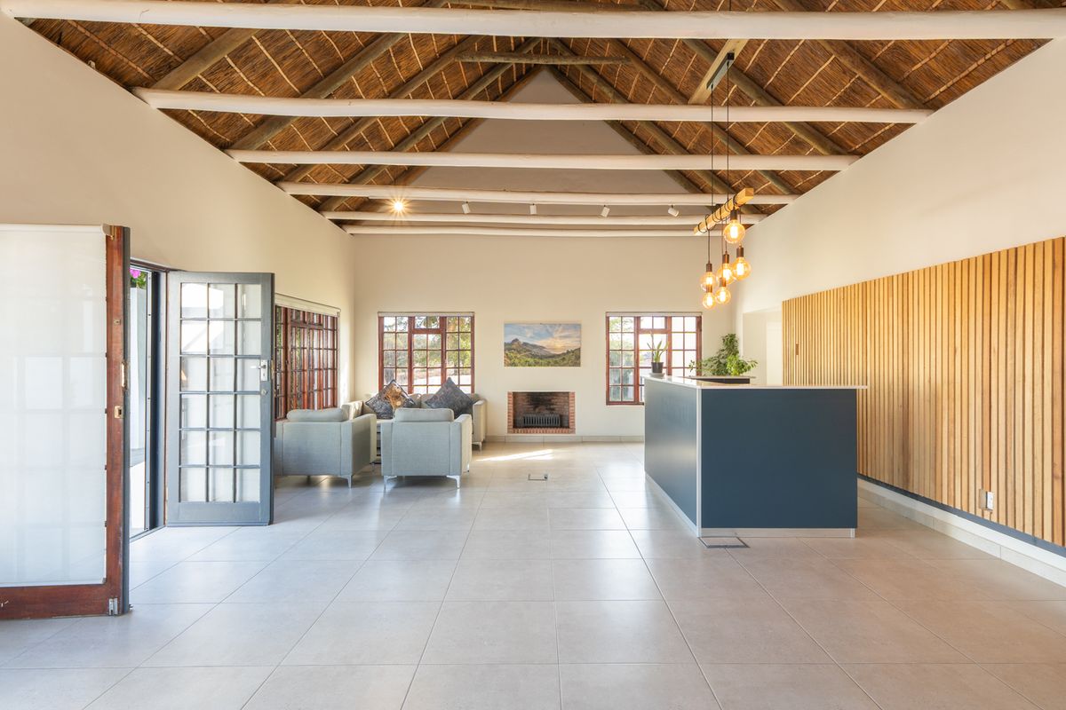 Spacious living area featuring a high thatched ceiling with exposed timber beams, tiled floors, a built-in fireplace, and modern timber slat wall detailing.