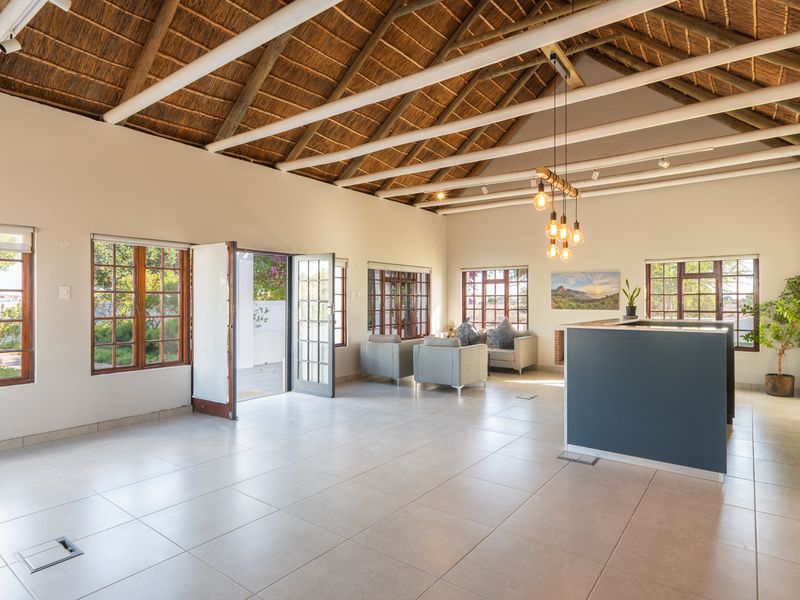 Spacious open-plan living area featuring a high thatched roof with exposed rafters, tiled flooring, and large timber-framed windows providing ample natural light.