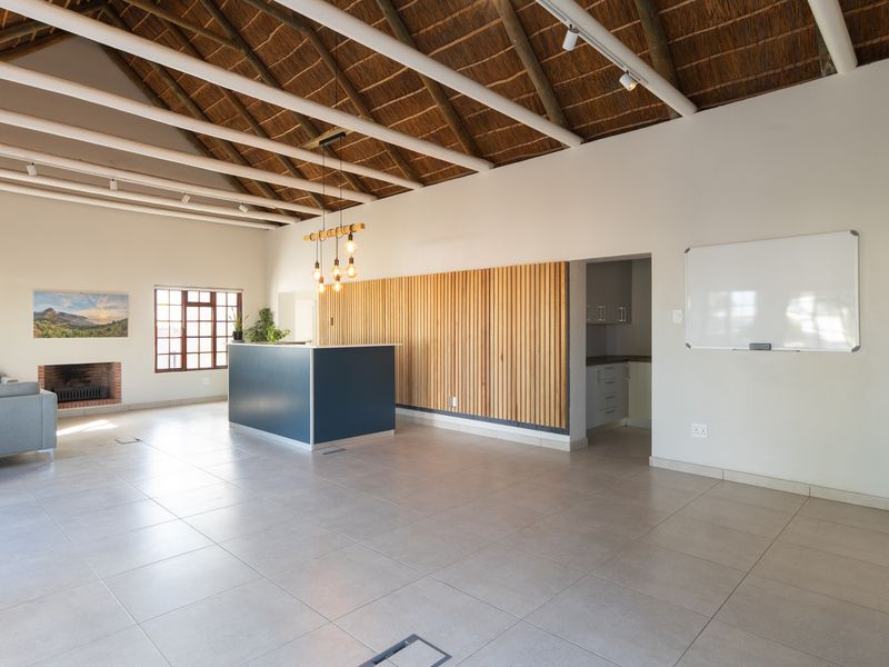 Spacious open-plan living area featuring a high thatched roof with exposed rafters, tiled floors, a built-in fireplace, and modern timber slat wall detailing.