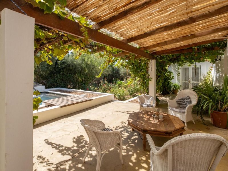 A covered outdoor patio featuring a timber pergola, concrete flooring, and direct access to a swimming pool and garden area.