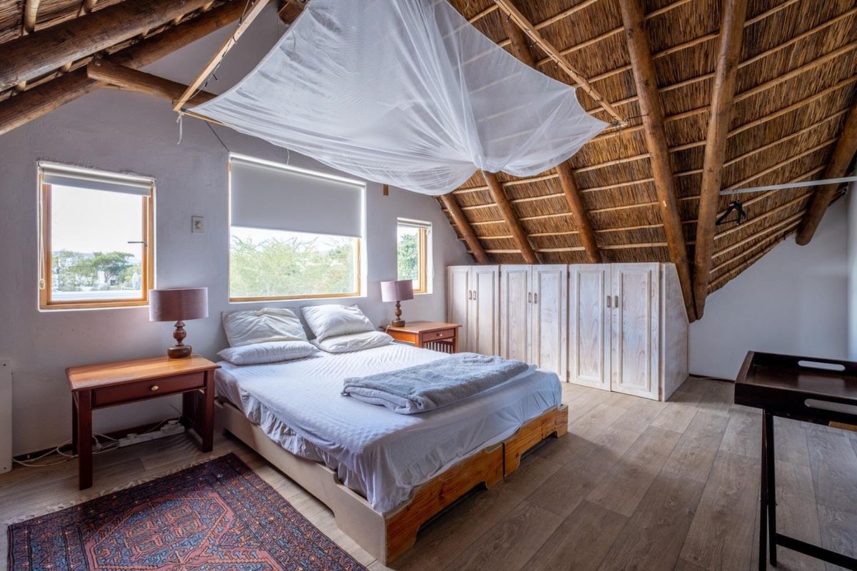 A cozy bedroom featuring a unique thatched roof with exposed timber rafters, built-in wooden cupboards, and laminate flooring.