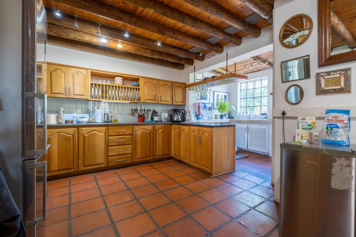 A rustic kitchen featuring exposed timber ceiling beams, terracotta floor tiles, wooden cabinetry, and granite countertops with a functional layout.