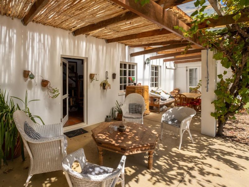 A charming covered patio area featuring a rustic timber pergola, concrete flooring, and direct access to the home's interior through a classic doorway.