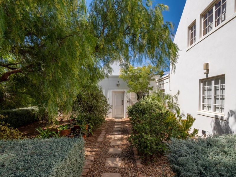 A charming front entrance featuring a stone pathway leading to a white door, surrounded by mature landscaping and a well-maintained exterior facade.