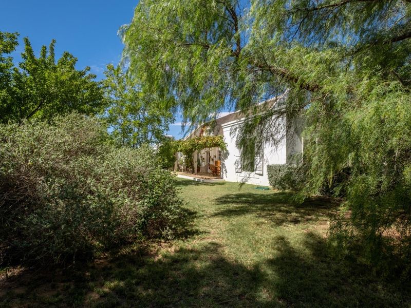 A view of the rear garden featuring a well-maintained lawn, mature trees, and a covered patio area attached to the main house structure.