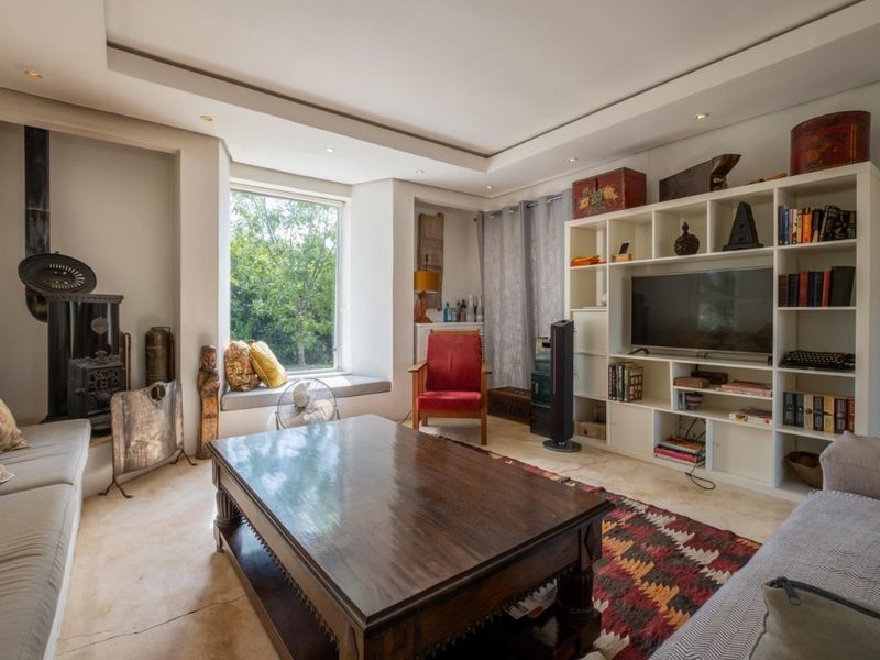 A cozy living room featuring a cast iron fireplace, stone flooring, recessed ceiling lighting, and a built-in window seat overlooking the garden.