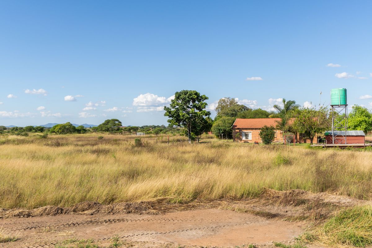 A wide-angle view of a rural farm property featuring a brick dwelling, a water storage tank on a stand, and expansive open grassland.