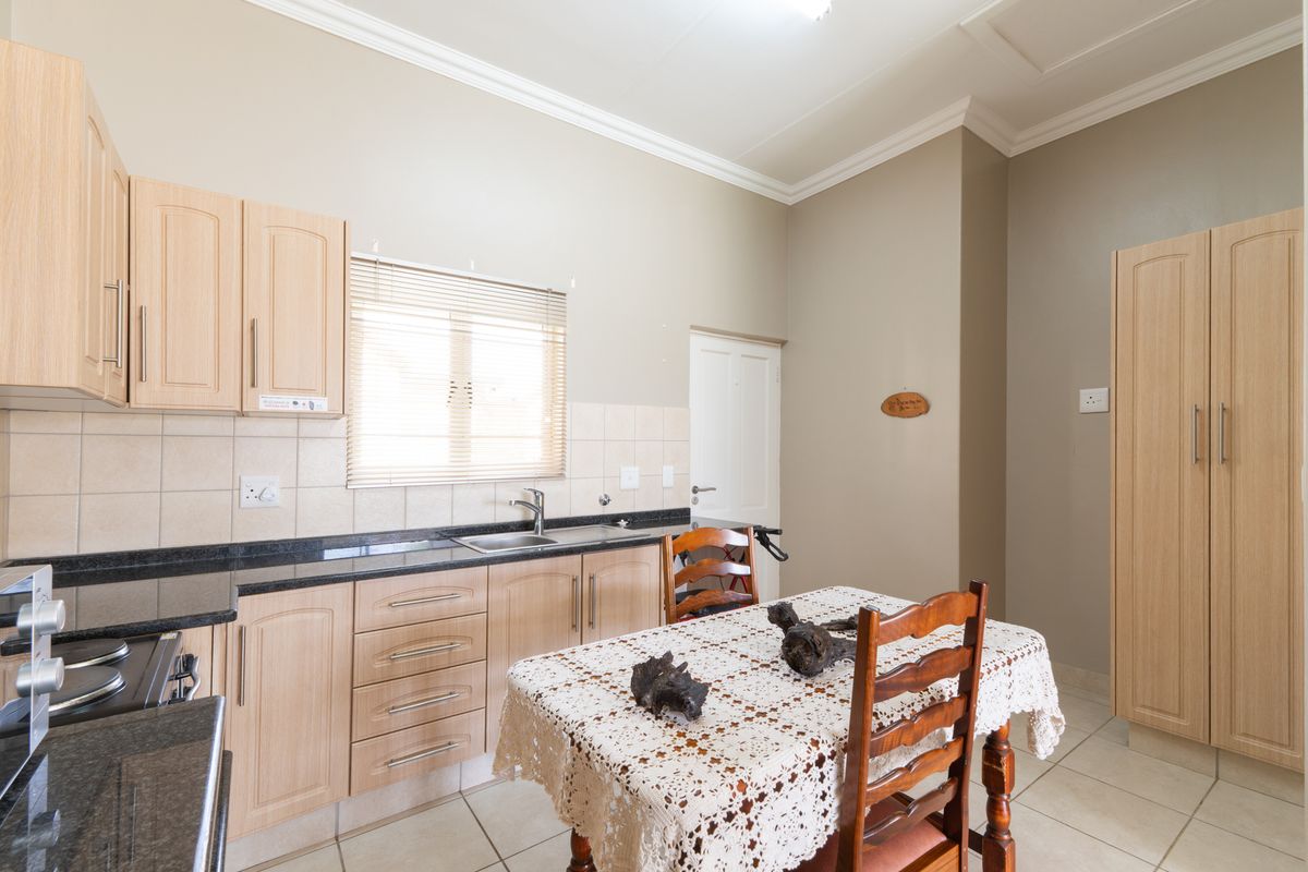 A functional kitchen featuring light wood cabinetry, dark granite countertops, tiled backsplash, and integrated storage, with an adjacent dining area.