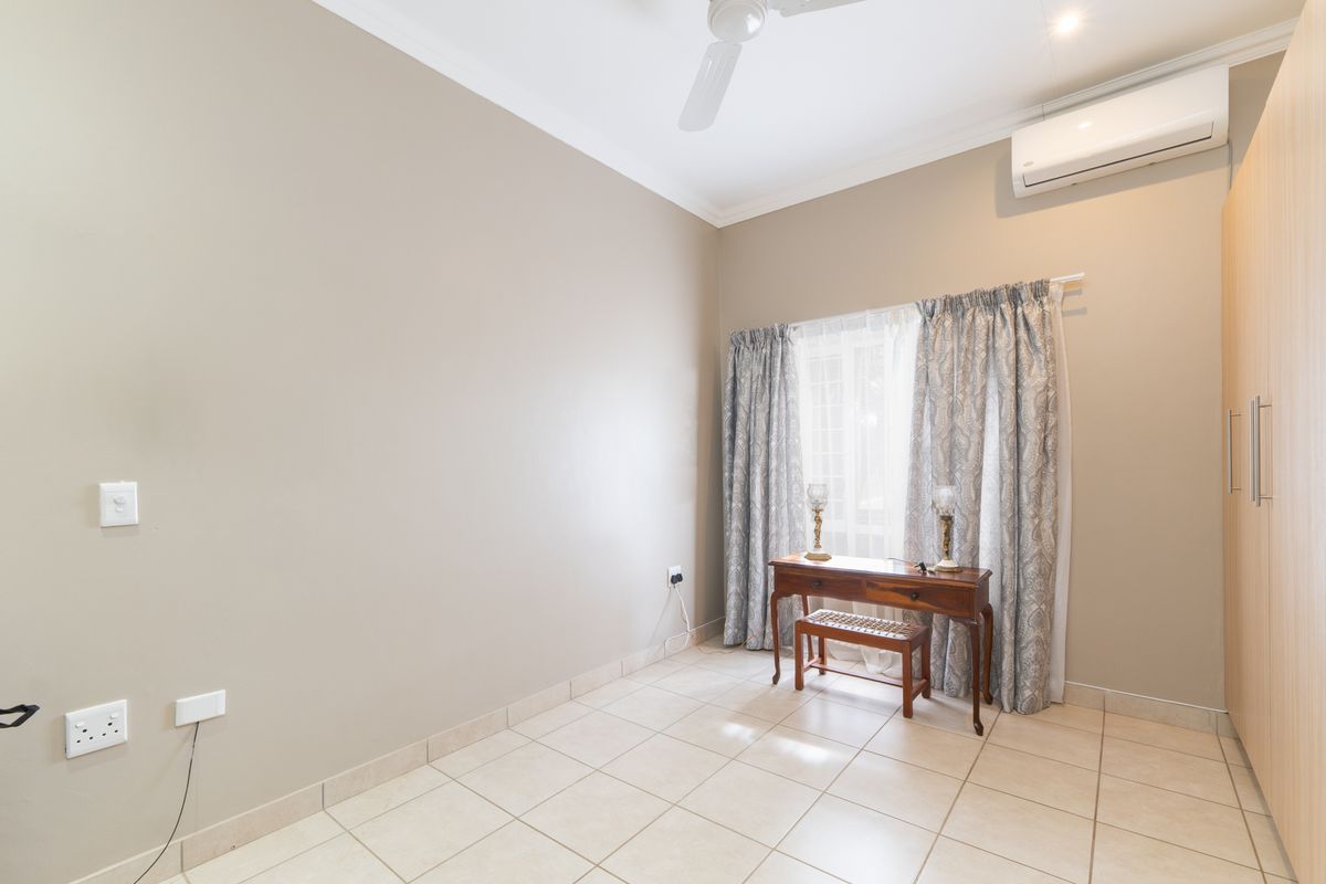 A bright bedroom featuring tiled flooring, built-in cupboards, a ceiling fan, and a wall-mounted air conditioning unit.