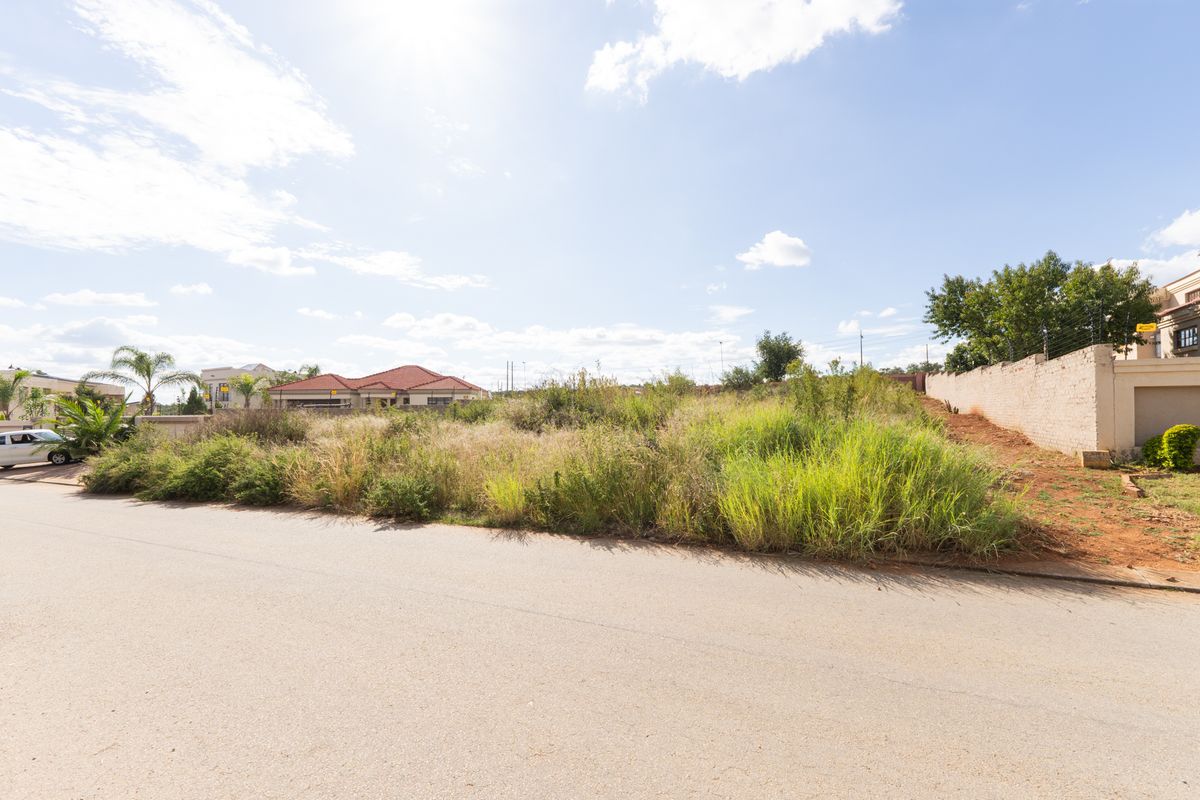 A vacant residential plot featuring natural vegetation, bordered by a perimeter wall, offering a clear site for future development.