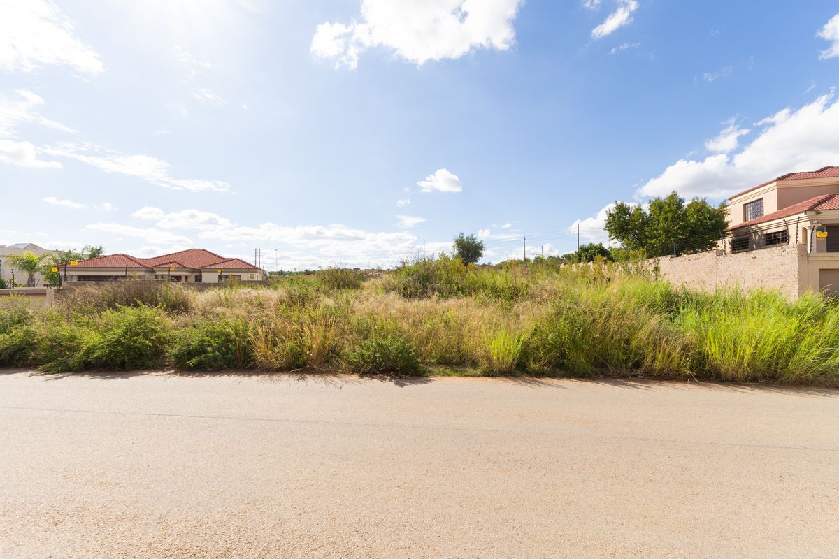 A vacant residential plot situated between existing homes, featuring natural vegetation and street-level access in a developed neighborhood.