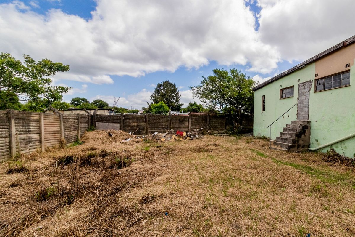 Rear exterior view of the property featuring a large, unmaintained yard area, concrete boundary wall, and external staircase access to the building.