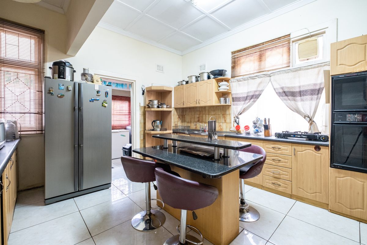 A functional kitchen featuring light wood cabinetry, granite countertops, a central breakfast bar, and tiled flooring with integrated oven and sink.