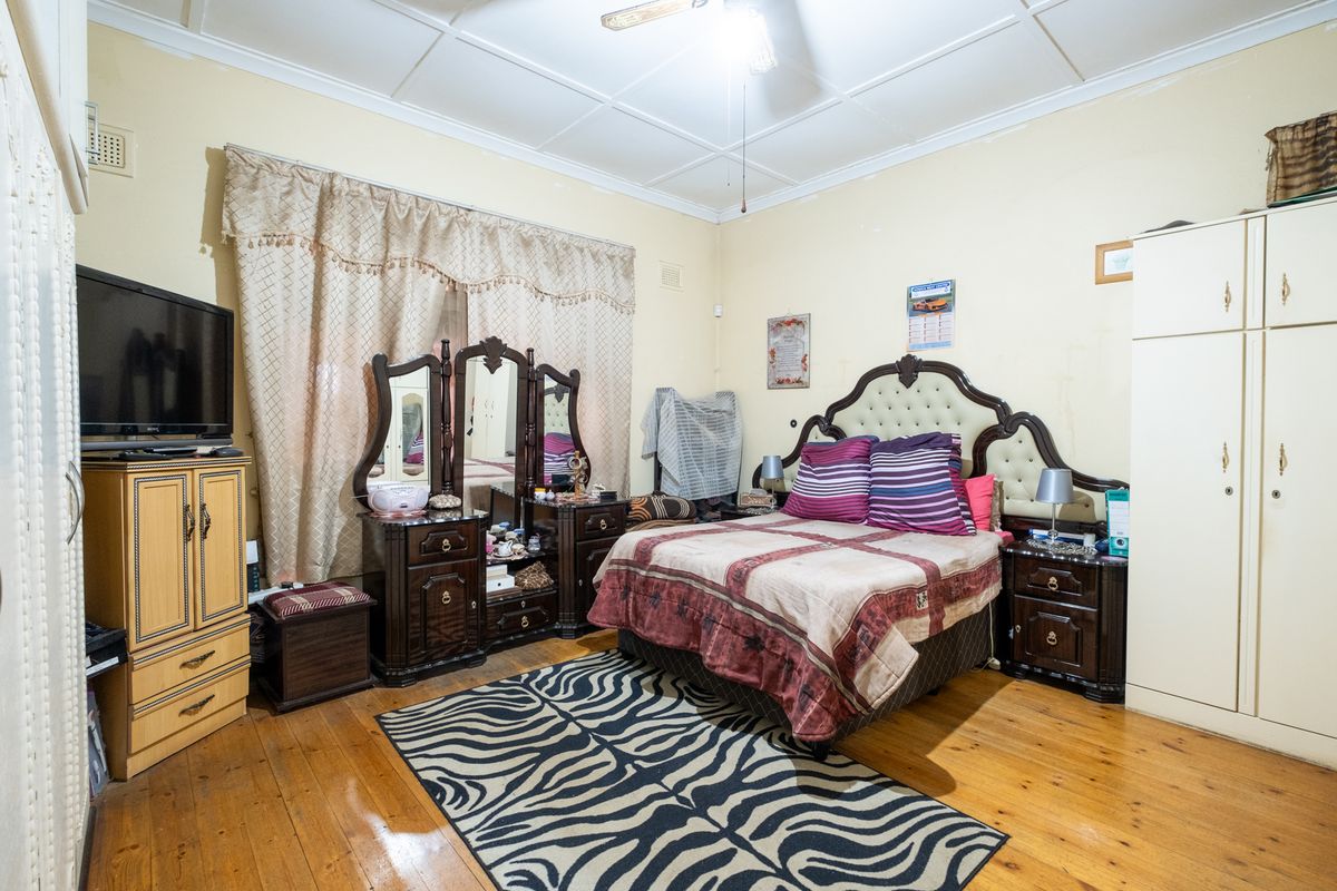 A bedroom featuring polished timber flooring, a ceiling fan, and built-in wardrobe storage, showing signs of wear on the ceiling and walls.