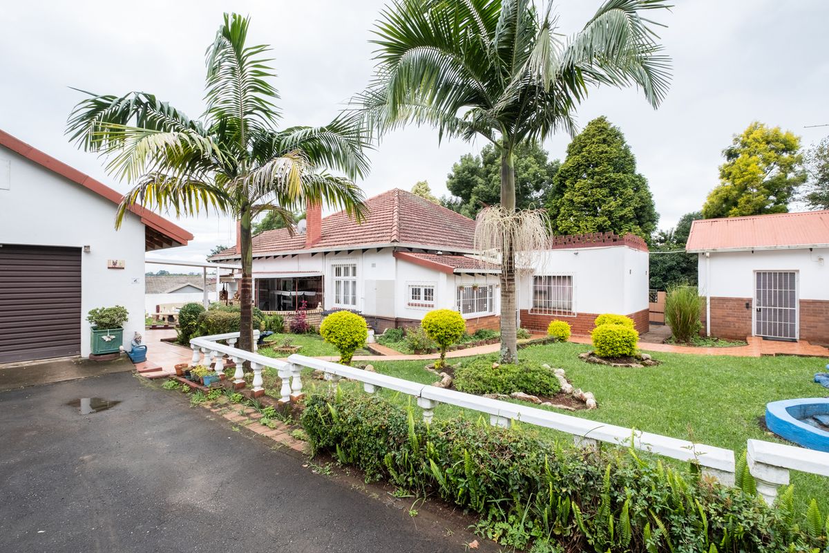 Rear view of the property featuring a landscaped garden, paved driveway, detached garage, and traditional brick and tile construction.