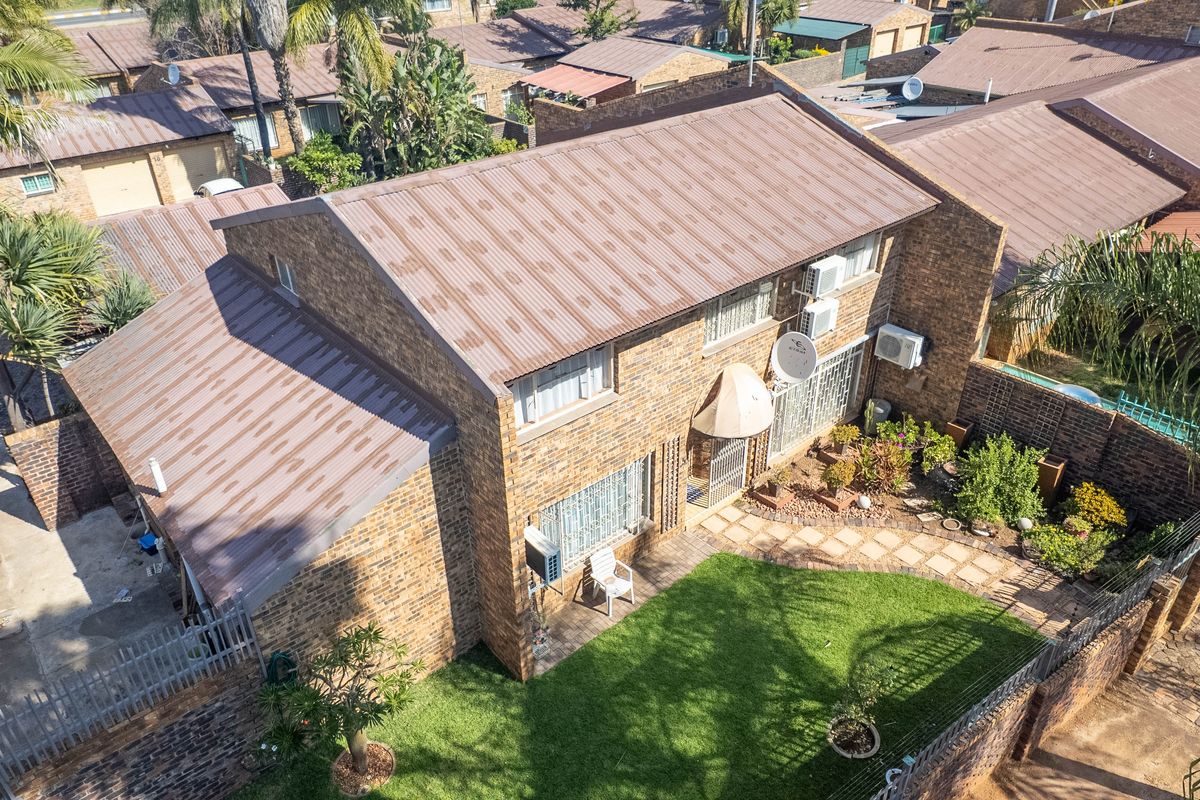 Aerial view of a brick townhouse featuring a metal roof, private garden, paved walkway, and security bars on windows.