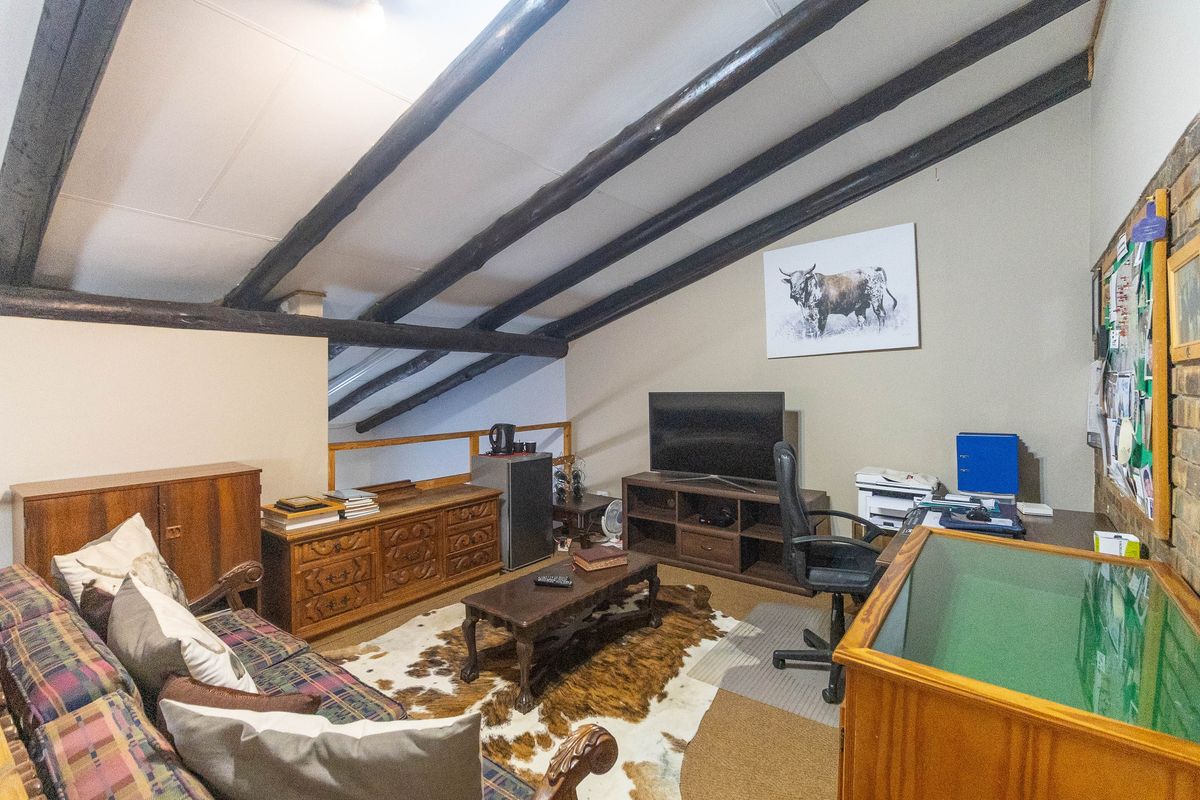A loft-style living area featuring exposed timber ceiling beams, raked ceilings, and a brick feature wall, providing a cozy and character-filled space.
