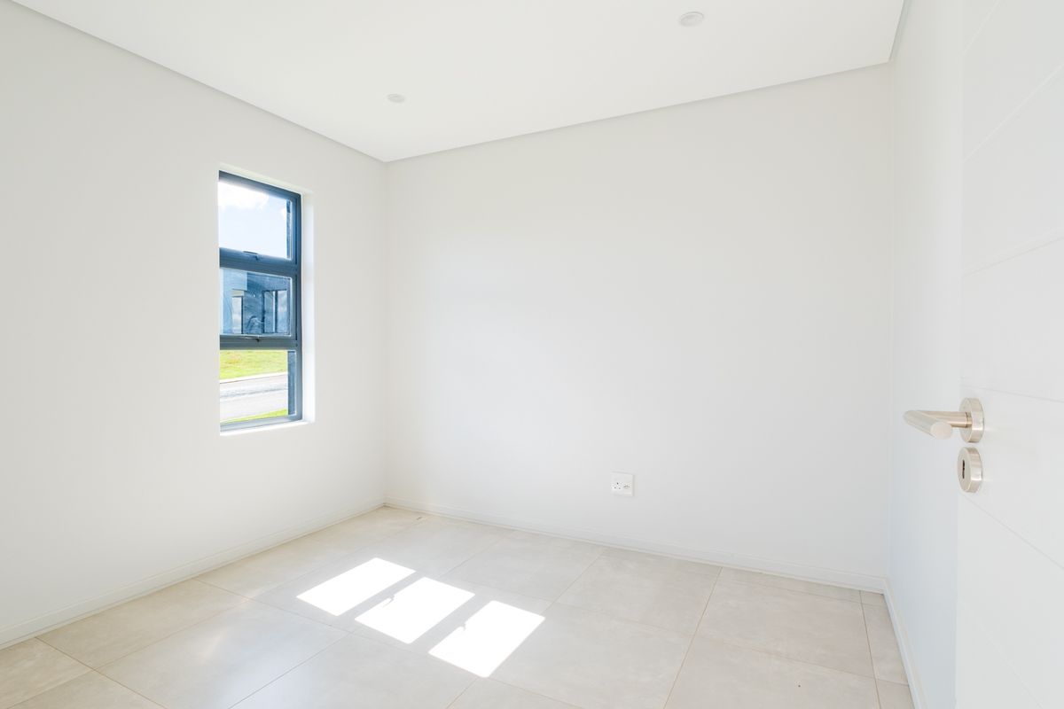 A bright, empty bedroom featuring neutral tiled flooring, modern recessed lighting, and a large window providing natural light.