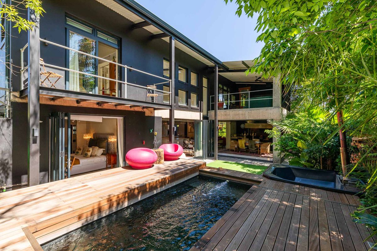 A modern multi-level restaurant exterior featuring a wooden deck, swimming pool, and seamless indoor-outdoor flow through large folding glass doors.