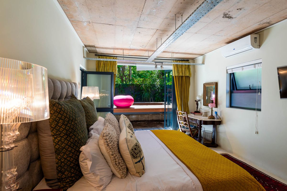 A bedroom featuring an industrial-style exposed concrete ceiling, wall-mounted air conditioning unit, and large glass doors opening onto a private outdoor patio area.
