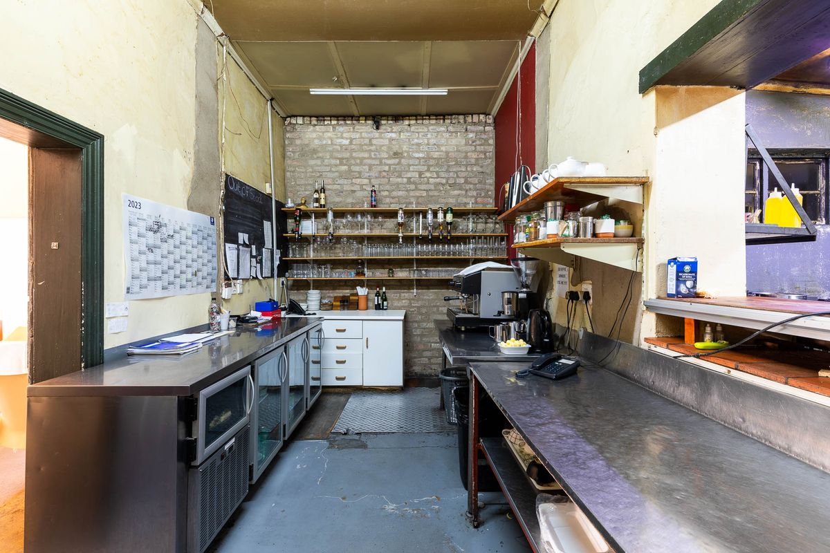 A functional commercial kitchen prep area featuring stainless steel work surfaces, open shelving, and exposed brick wall detailing.