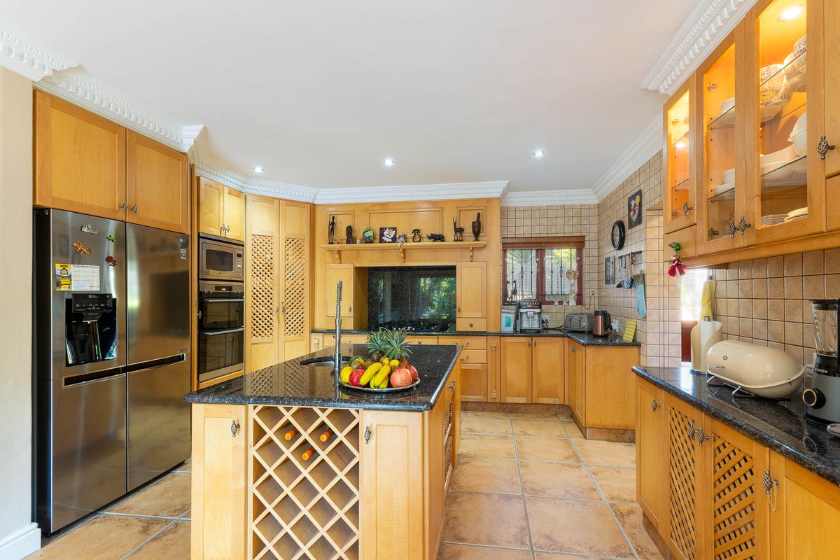 Spacious kitchen featuring light wood cabinetry, granite countertops, a central island with integrated wine storage, and tiled flooring throughout.