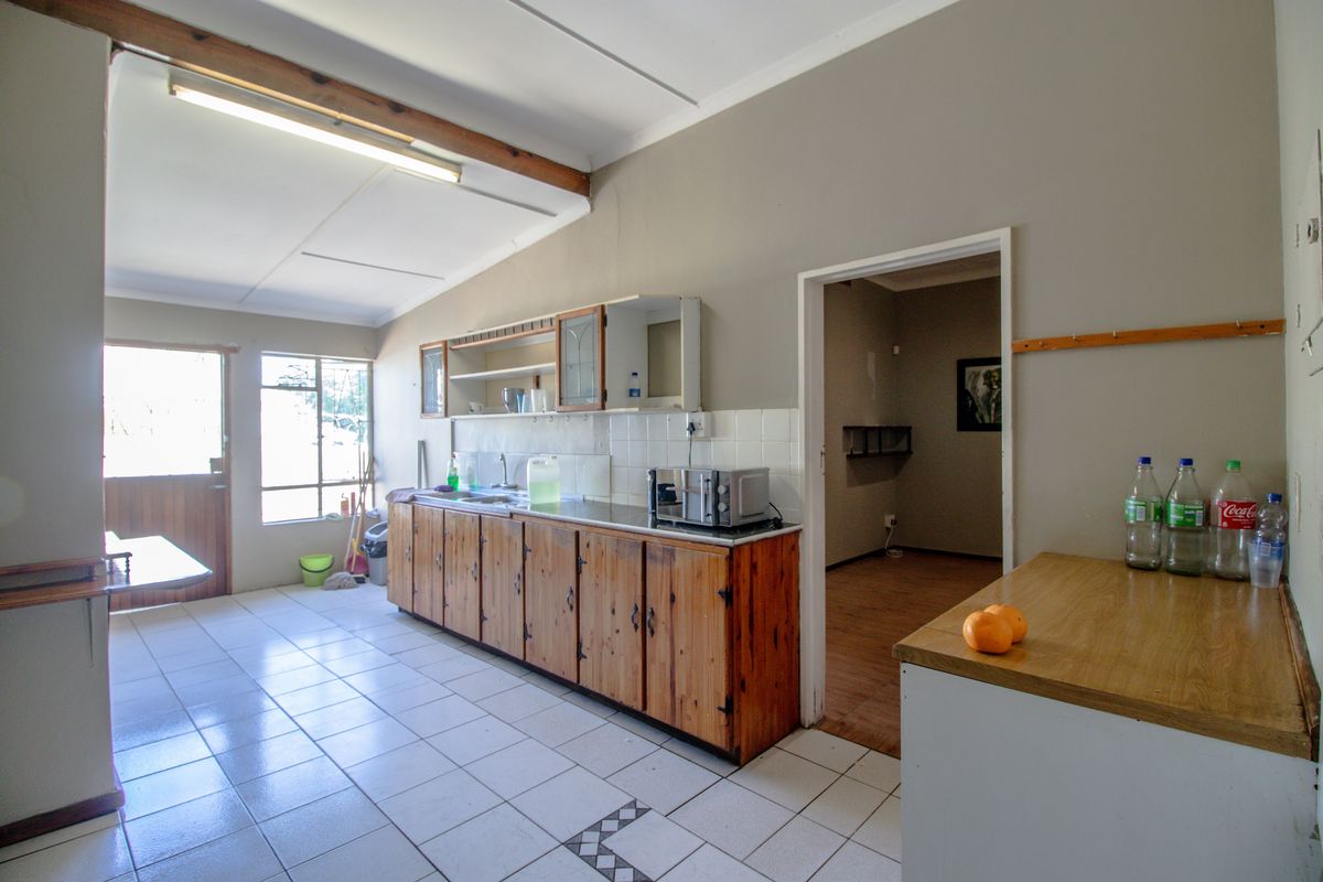 A functional kitchen area featuring wooden cabinetry, tiled flooring, and a tiled backsplash, providing a practical workspace with direct access to an adjacent room.
