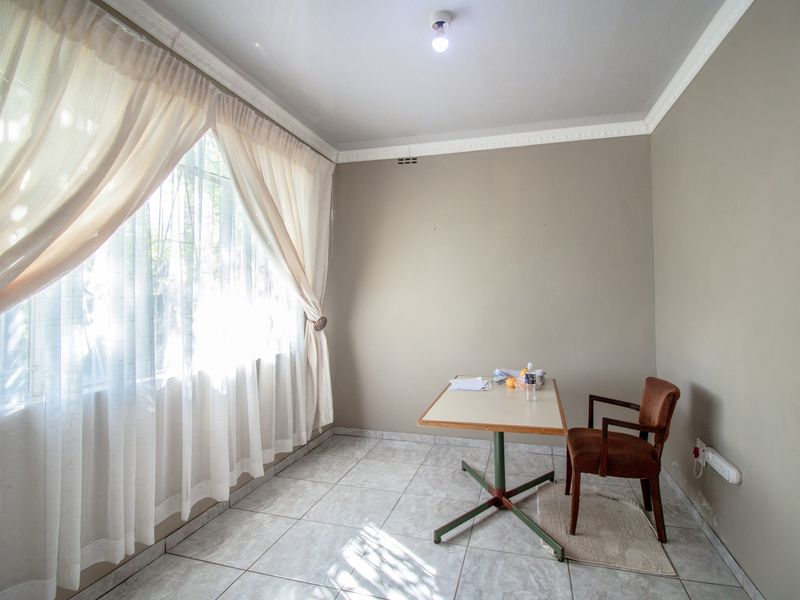 A simple, tiled room featuring large windows with curtains, suitable for use as a home office or small study area.
