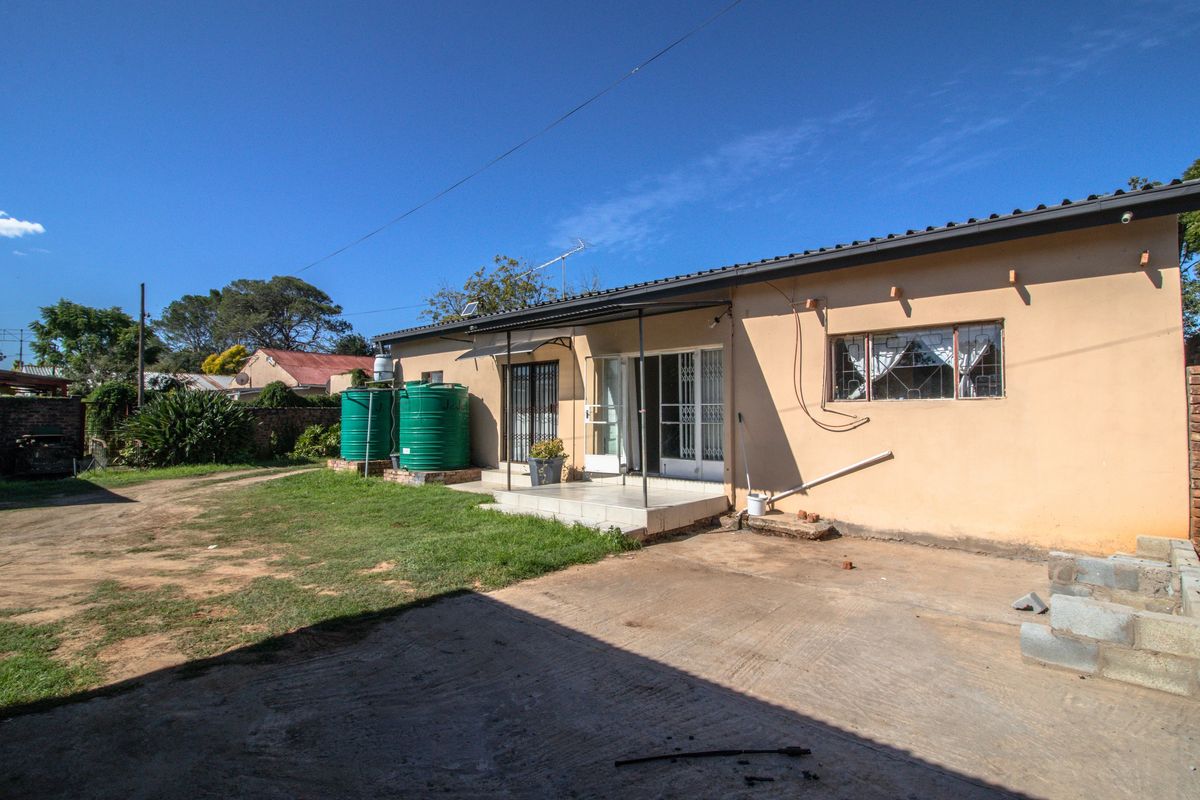 Rear view of the property featuring a paved patio area, water storage tanks, and a spacious backyard with a concrete driveway.