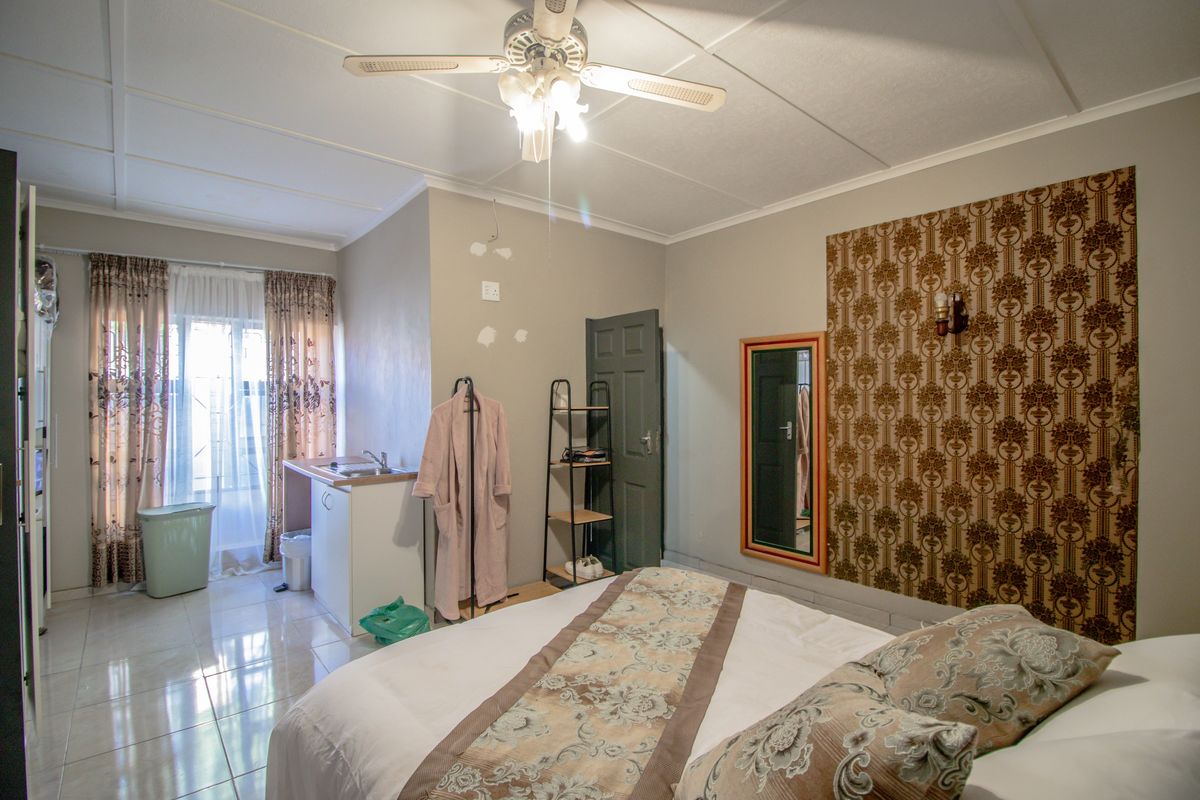 A bedroom featuring tiled flooring, a ceiling fan, and a small built-in kitchenette area with a sink.