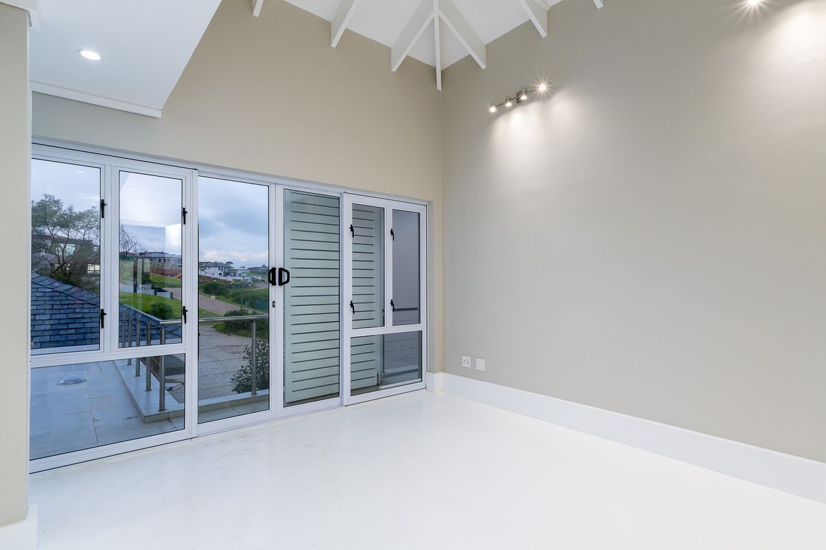 A bright, empty bedroom featuring high vaulted ceilings, neutral walls, and large sliding glass doors that open onto a balcony with scenic views.